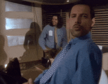 a man in a blue shirt and tie is looking at himself in the mirror