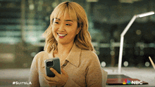 a woman is smiling while holding a cell phone with #suitsla written on the bottom