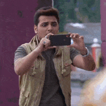 a man in a vest is taking a picture of himself with a cell phone .