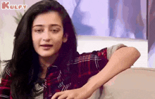 a woman in a plaid shirt is sitting on a couch and making a face .
