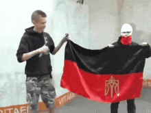 a man is holding a red and black flag with a gold symbol on it