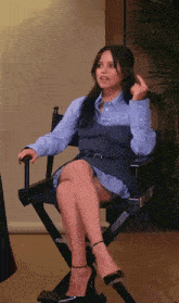 a woman in a blue dress is sitting in a director 's chair with her legs crossed