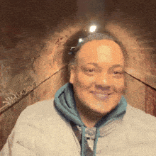 a man wearing a gray jacket and a blue hoodie is smiling