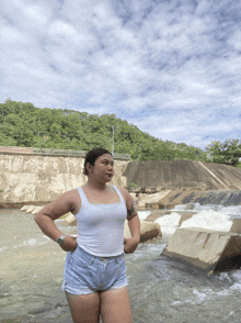 a woman in a white tank top and shorts is standing in a river