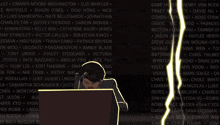 a man sits in front of a wall of names including patrick bryson and amber blade
