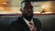 a man in a suit and tie sits in a booth with a bet logo on the bottom