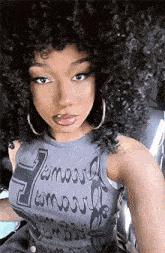 a woman with curly hair is taking a selfie while wearing a gray tank top and hoop earrings .