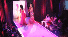 a couple of women walking down a runway with purple lights