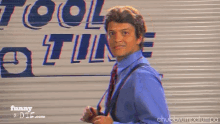 a man in a blue shirt and tie is standing in front of a tool store sign
