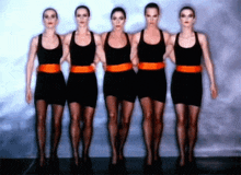 a group of women in black dresses and orange belts are standing in a line