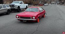 a red car is driving down a street with a white truck in the background