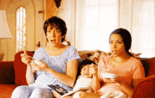 three women are sitting on a couch with a baby and one of them is eating cereal