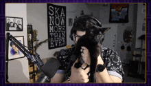 a man holds a black cat in front of a sign that says ska now more than ever