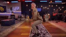 a man is squatting on a rug in a room with a band playing in the background .