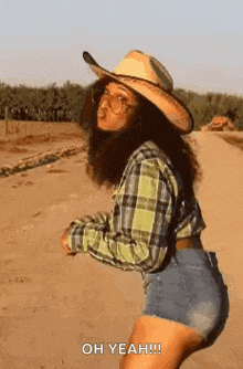 a woman wearing a cowboy hat and plaid shirt is dancing on a dirt road .