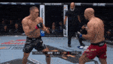 two men are fighting in a boxing ring and one of them is wearing shorts with the word ufc on them