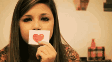 a girl holding a piece of paper with a heart on it in front of her mouth