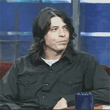 a man in a black shirt is sitting at a table with a cup of coffee .