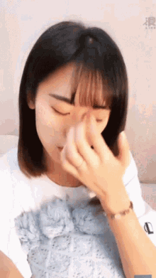 a woman is covering her nose with her hands and has a bracelet on her wrist