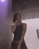 a woman in a black tank top is singing into a microphone on a stage