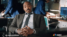 a man in a suit and tie sits in a chair with a nbc logo in the corner