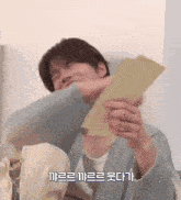 a man in a blue sweater is holding a piece of paper with korean writing on it .