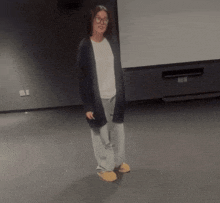 a woman wearing glasses and a cardigan is standing in a dark room