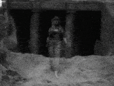 a black and white photo of a woman standing in front of a building in the desert .
