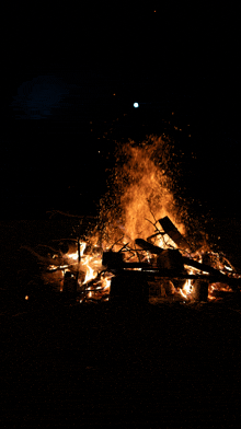 a large fire is lit up in the dark with a full moon in the background