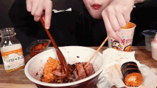 a person eating a bowl of food with chopsticks next to a bottle of orange sauce