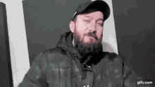 a man with a beard and a hat is sitting in front of a black and white wall .