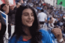 a woman wearing sunglasses and a blue shirt is smiling in front of a crowd of people