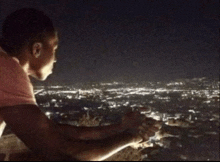 a man in a pink shirt is looking out over a city at night