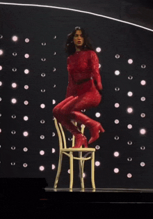 a woman in a red jumpsuit is sitting on a chair on a stage