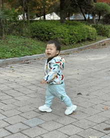a little boy wearing a colorful jacket is walking down a brick sidewalk