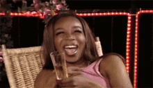 a woman is laughing while holding a glass of wine .