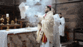 a priest stands in front of a table with a white cloth on it