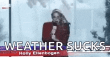a woman is holding a microphone in front of a sign that says `` weather sucks `` .