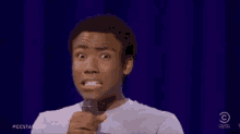 a man is making a funny face while standing in front of a microphone on a stage .