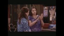 two girls are standing next to each other in front of a refrigerator and talking to each other .