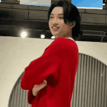 a man in a red sweater is standing with his arms crossed .