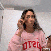 a woman wearing a pink shirt that says ot20 on it is applying makeup