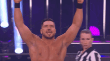 a shirtless wrestler with his arms in the air and a referee in the background