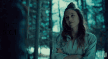 a woman with her arms crossed in a dark forest with the letters hw on the bottom right
