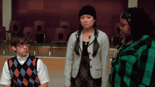 a man wearing glasses and a plaid vest is standing next to two women