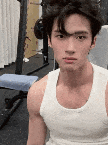 a man in a white tank top is sitting in a gym .