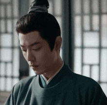 a man with a bun on his head is wearing a green shirt and looking down .