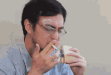 a man eating a sandwich with two cigarettes sticking out of his nose