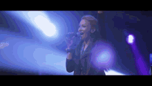 a woman singing into a microphone on a stage with blue lights behind her