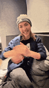 a woman wearing a beanie and a blue sweater is sitting on a bed